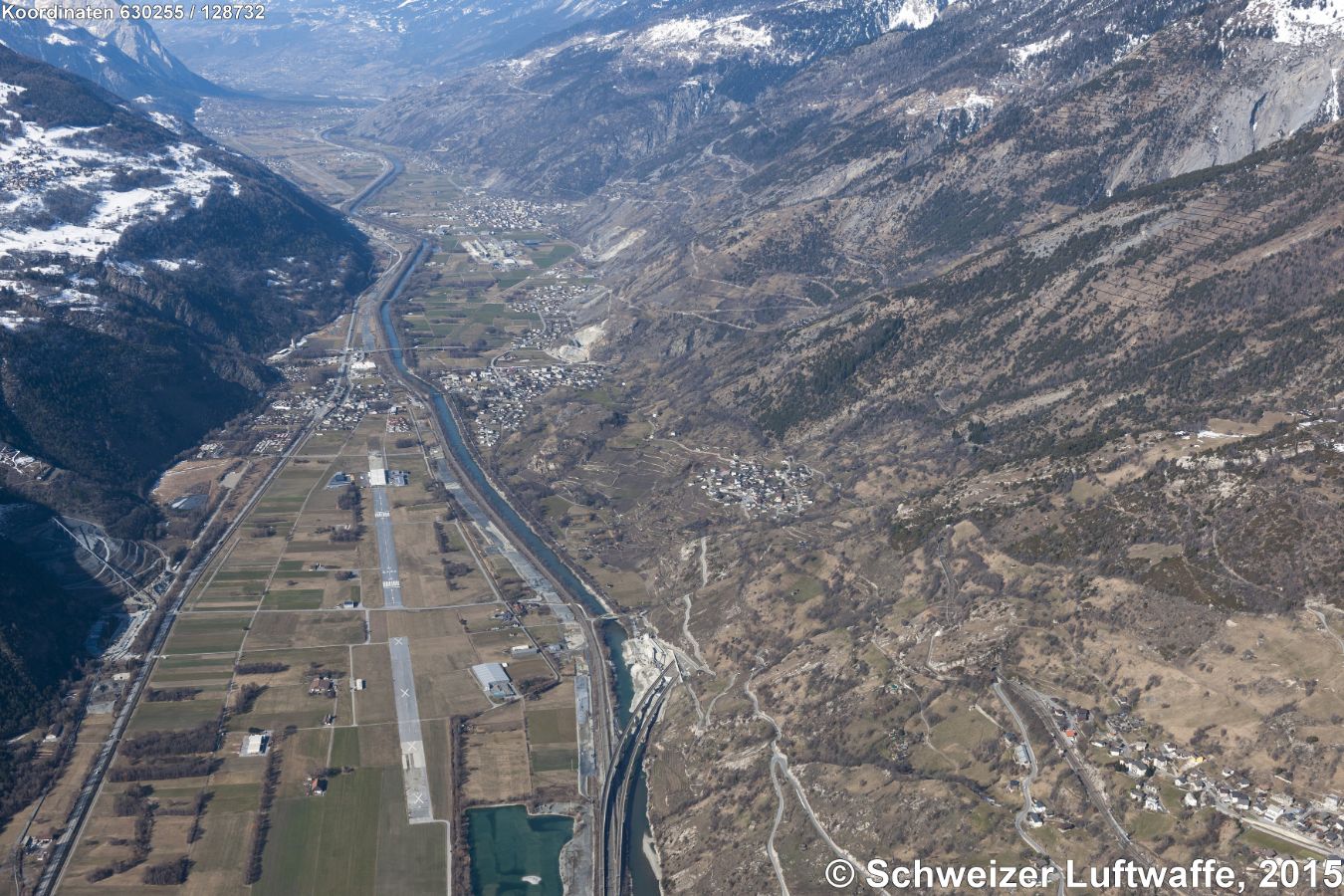 Lötschberg Basistunnel, Südportal am untern Bildrand (Position 2'630'257.64, 1'128'828.19) SE von St. German (VS). - Bahnverbindung von Frutigen (BE) nach Raron (VS) mit einer Tunnellänge von 34.6 Km; in Betrieb genommen am 16. Juni 2007. - Blick Rhone-abwärts Richtung W; Siedlung NW des Portals: St. German, weiter rhoneabwärts: Raron. Links der Rhone: ehemaliger Militärflugplatz, heute durch die Oberwalliser Fluggruppe privat genutzt.